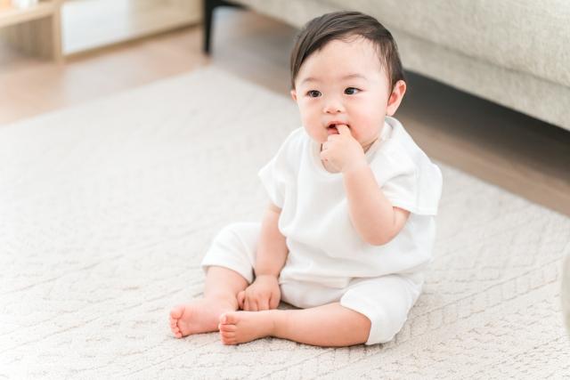 指をくわえて床に座る赤ちゃん