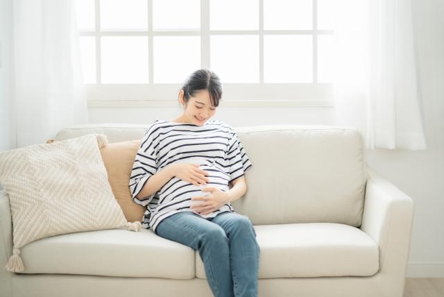 ソファに座りおなかに手を添えてほほえむ妊婦さん