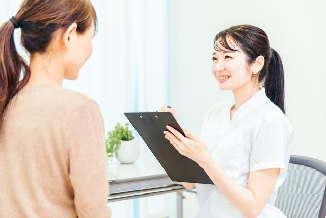 クリップボードを手に女性の相談を聞く医療スタッフ